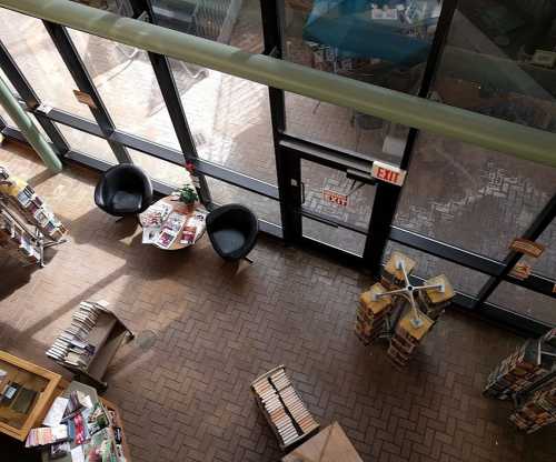 Aerial view of a library entrance with two chairs, a table of magazines, and bookshelves in the background.