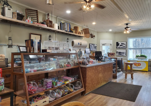 A cozy shop interior featuring a display case of candies, a wooden counter, and shelves with various items.