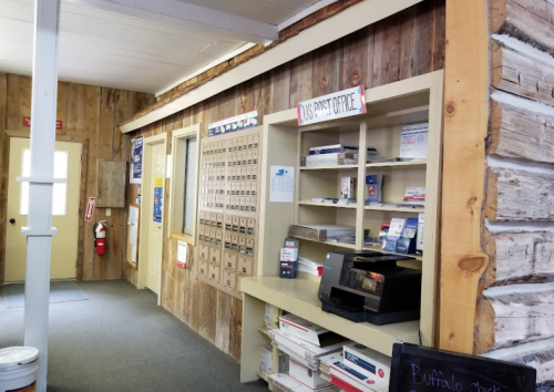 Interior of a rustic post office with wooden walls, mailboxes, and a service counter.