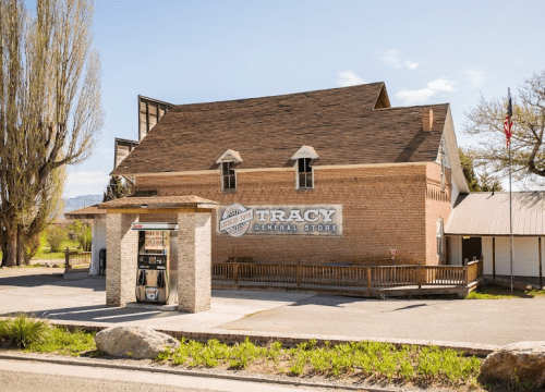 A brick building with a sign reading "Tracy General Store" and a small gas station in front, set against a clear sky.