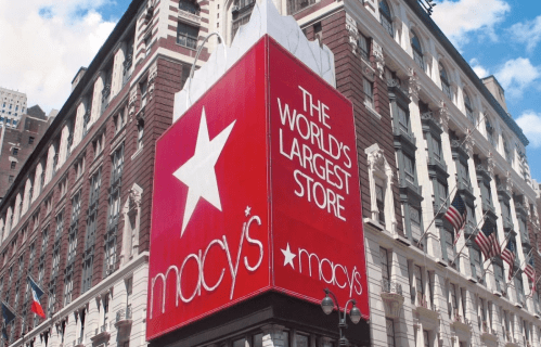 Macy's storefront with a large sign reading "The World's Largest Store" against a blue sky.