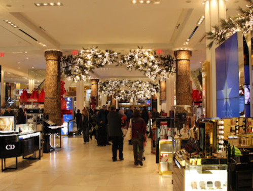 A bustling department store interior decorated with festive lights and displays, featuring shoppers and holiday decor.