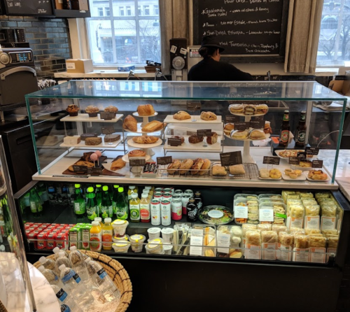 Display case filled with various baked goods and drinks, including pastries, cakes, and bottled beverages.