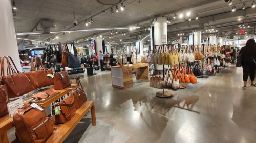 A spacious store displaying a variety of handbags and accessories on shelves and racks, with shoppers browsing.