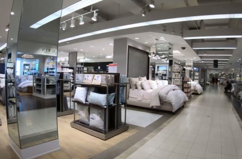 A spacious home goods store featuring bedding displays, mirrors, and neatly arranged products on shelves.