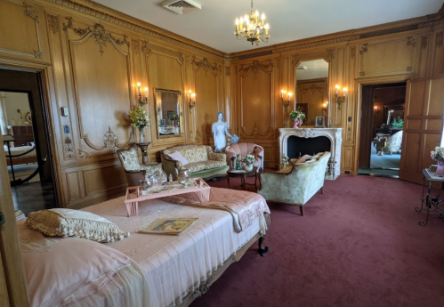 Elegant bedroom with wooden paneling, vintage furniture, a chandelier, and a cozy seating area.