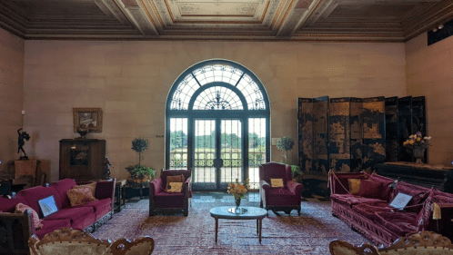 Elegant room with red sofas, a round table, and large windows, showcasing a view of the outdoors.