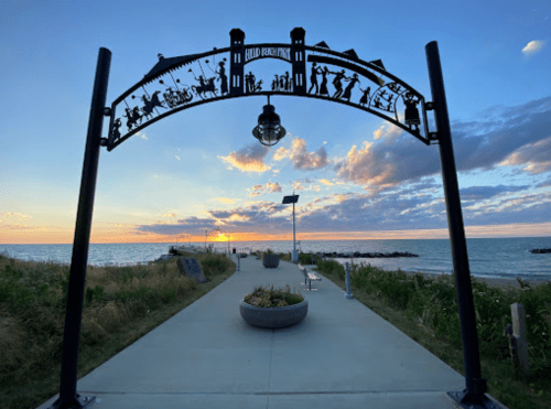 Silhouette archway at sunset over a pathway by the lake, with clouds and water in the background.