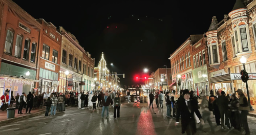 A bustling street at night, lined with historic buildings and festive lights, filled with people enjoying the atmosphere.