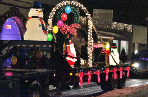 A festive parade float featuring a snowman, Santa, and colorful lights, set against a nighttime backdrop.