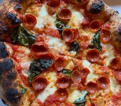 A close-up of a pepperoni pizza with melted cheese and fresh basil on a charred crust.