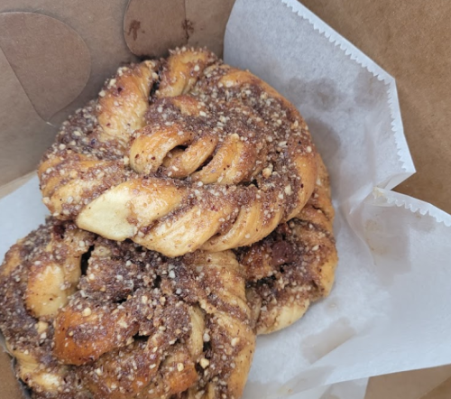 Two cinnamon rolls with a crunchy topping, nestled in a paper bag with a parchment liner.