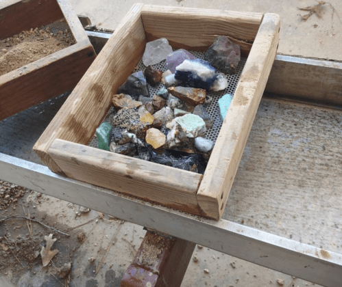 A wooden box filled with various colorful rocks and minerals, resting on a metal surface.