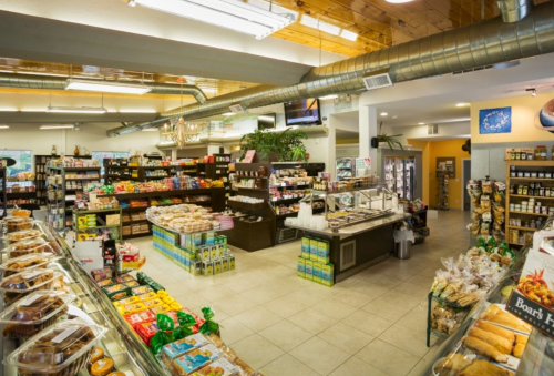 A well-stocked grocery store interior with shelves of snacks, drinks, and baked goods, featuring a bright, open layout.