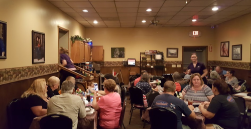 A busy restaurant interior with diners at tables, a server walking upstairs, and decor on the walls.