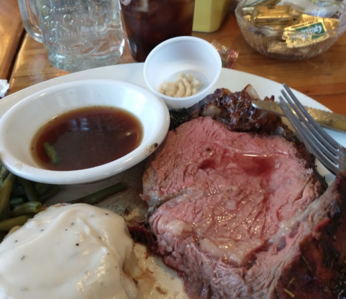 A plate featuring a slice of prime rib, green beans, mashed potatoes with gravy, and a small dish of horseradish.