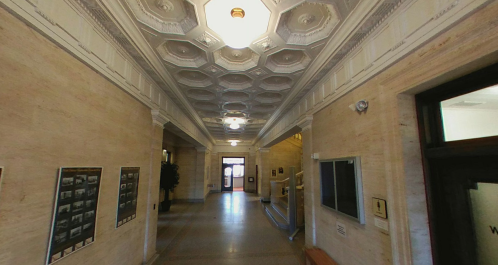 A long hallway with ornate ceiling details, light fixtures, and framed photos on the walls.