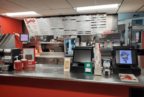 A fast-food counter with menus, cash registers, and condiments in a brightly lit restaurant.
