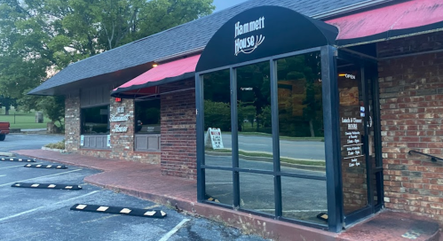 Exterior view of Hammett House restaurant with a brick facade, large windows, and a red awning. Parking area visible.