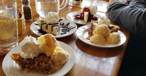 A table with four dessert plates: pie with whipped cream, chocolate cake, cheesecake with berries, and scoops of ice cream.