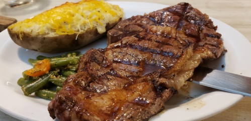 A plate featuring a grilled steak, baked potato with cheese, and green beans with carrots.