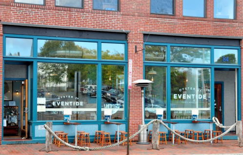 Exterior of Eventide Oyster Co. in Portland, featuring large windows and outdoor seating. Brick building with blue accents.