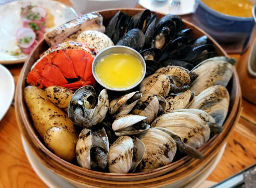 A wooden bowl filled with various seafood, including lobster, clams, mussels, and a small cup of melted butter.