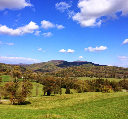 A scenic landscape featuring rolling hills, lush green fields, and a blue sky with fluffy clouds.