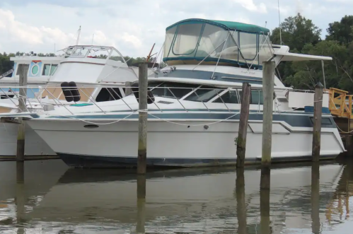 A white motorboat docked at a marina, surrounded by water and other boats in the background.