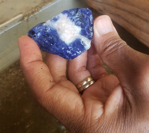 A hand holding a blue mineral specimen with white veins, set against a blurred background.