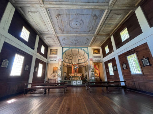 Interior of a historic chapel featuring wooden walls, a painted ceiling, and an altar at the front.