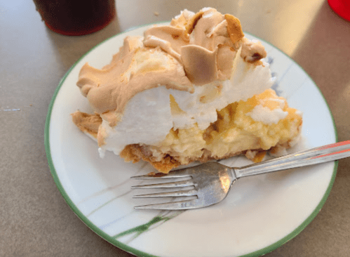 A slice of banana cream pie topped with fluffy meringue on a white plate with a fork beside it.