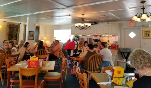 A busy restaurant interior with families and groups dining at wooden tables, bright lighting, and a cozy atmosphere.