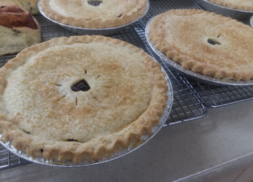 Three freshly baked pies cooling on a wire rack, with golden crusts and a shiny, sugared top.
