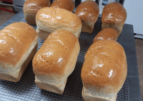 Freshly baked loaves of bread cooling on a wire rack, with a golden-brown crust and shiny surface.