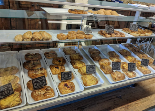 A display case filled with various baked goods, including pastries and donuts, each labeled with small signs.