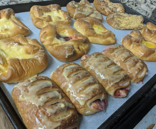 A tray of freshly baked pastries, including fruit-filled danishes and cream cheese rolls, drizzled with icing.