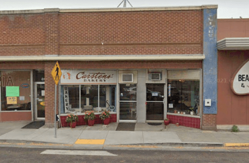 Exterior view of Carsten's Bakery, featuring a brick facade, large windows, and flower pots along the sidewalk.