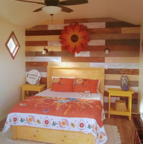 Cozy bedroom with a wooden bed, colorful bedding, and a decorative flower wall art. Bright yellow nightstands.