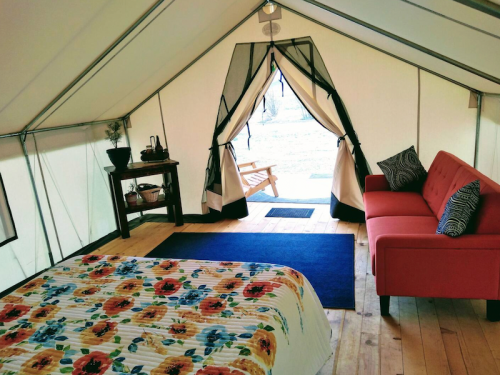 Cozy glamping tent interior with a floral bedspread, a red sofa, and an open entrance leading to the outdoors.