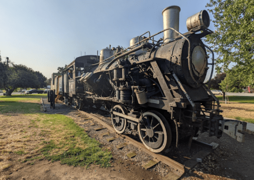 A vintage steam locomotive displayed outdoors, showcasing its large wheels and metal structure against a clear sky.