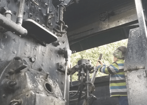 A child in a striped sweater explores the interior of a vintage steam locomotive.