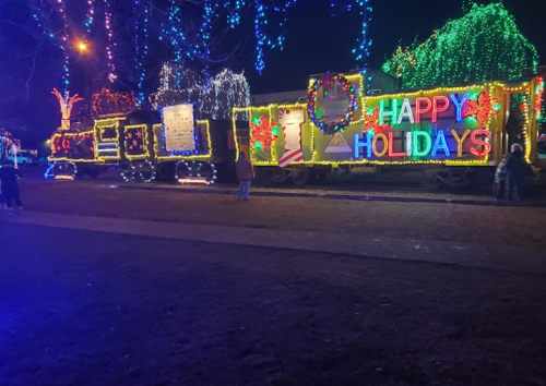 A brightly lit train decorated with colorful holiday lights and a "Happy Holidays" sign, set against a night sky.
