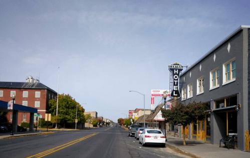 A quiet street scene featuring a hotel sign, parked cars, and buildings under a clear sky.