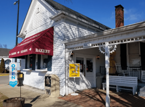 A charming white bakery with a red awning, open sign, and a welcoming porch.