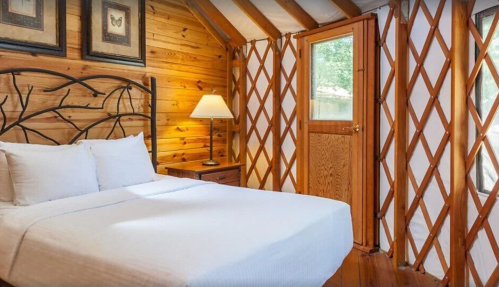 Cozy wooden bedroom with a double bed, lamp, and a door leading outside, featuring a rustic, cabin-like design.