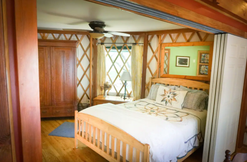 Cozy bedroom featuring a wooden bed, quilt, dresser, and unique lattice wall design. Natural light from a window.