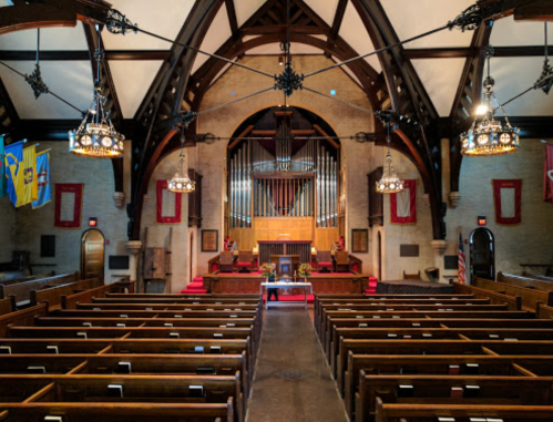 Interior of a church featuring wooden pews, a large organ, and decorative chandeliers under a vaulted ceiling.