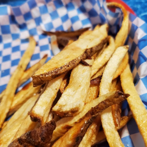 A basket of golden-brown French fries on blue and white checkered paper.