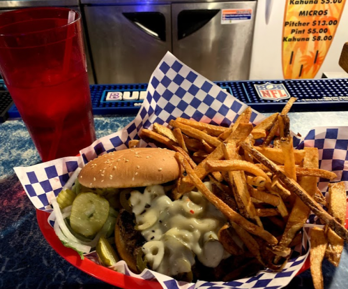 A plate of a burger with cheese, pickles, and a side of crispy fries, accompanied by a red drink.